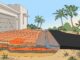 Terracotta pavers transition to asphalt beside palms and a drainage buffer.